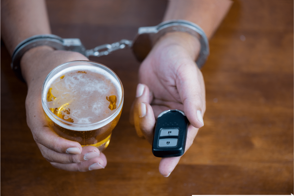 an handcuffed hand holding a car key and alcohol