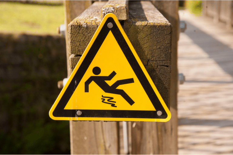 Yellow triangular sign with a slipping figure, indicating a slippery surface ahead on a wooden bridge.